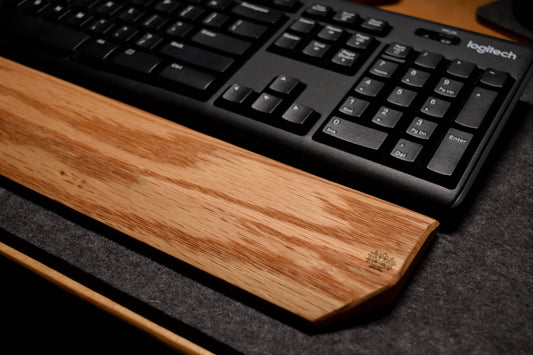 Keyboard on an oak wood wrist rest with a dark wool desk pad background.