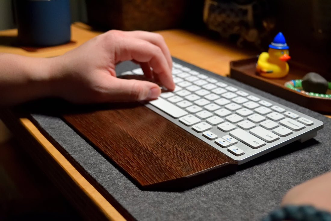 Lonoke Designs wenge keyboard wrist rest on a gray desk pad with a white and silver keyboard.