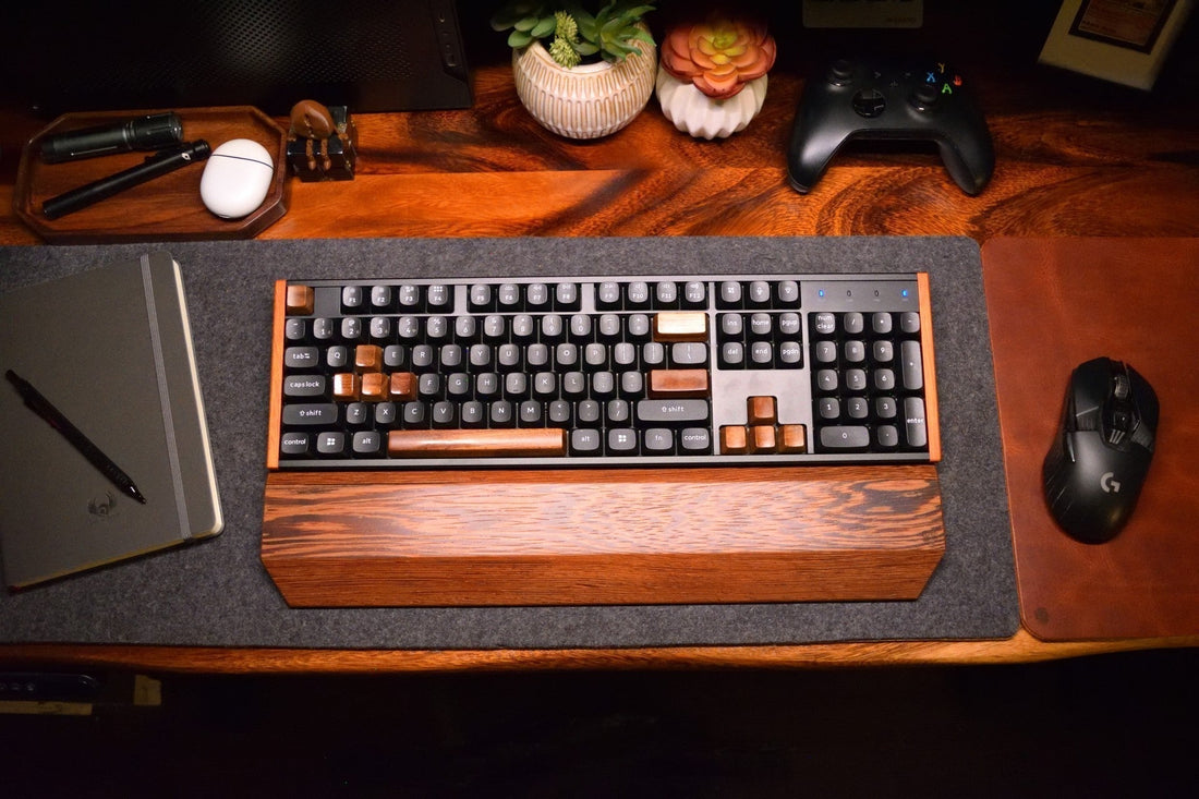 Overhead view of a desk setup with a Lonoke Designs wenge keyboard wrist rest and mechanical keyboard. Also has a brown leather mouse pad, walnut catchall tray and plants for decoration.
