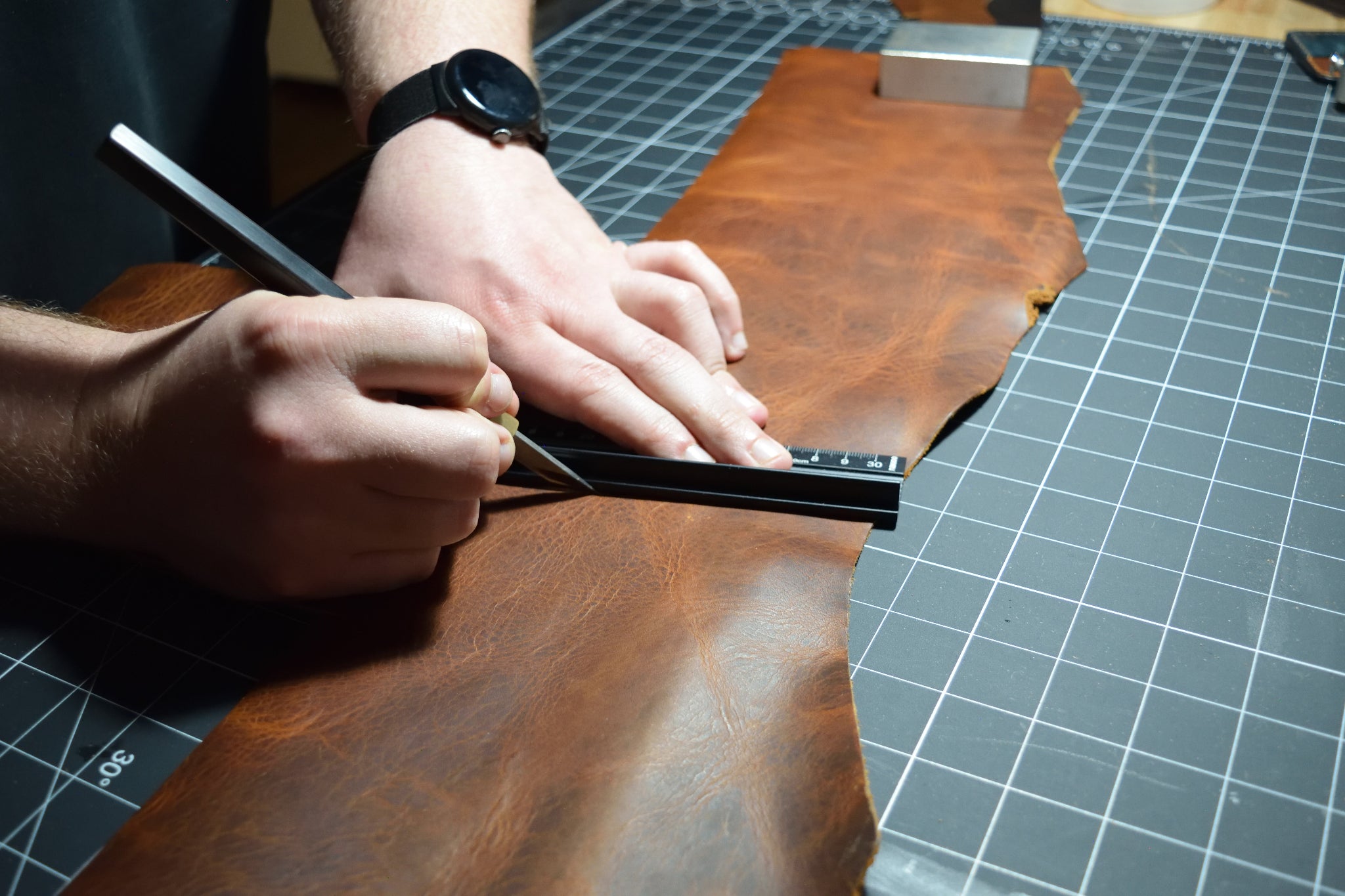 Person working on a leather project with a ruler on a grid surface in the Lonoke Designs workshop.