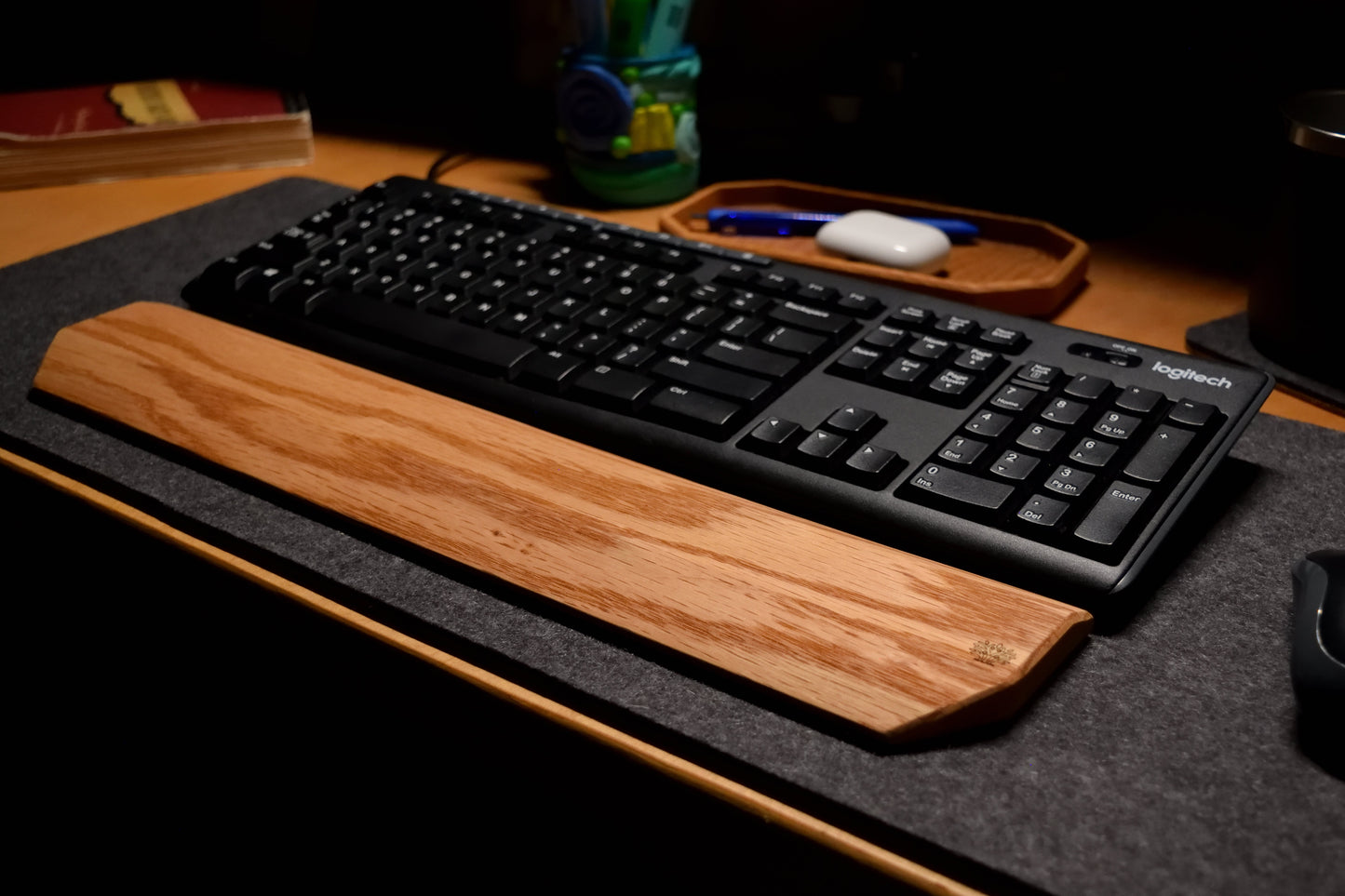 Black keyboard with an oak wooden wrist rest, with a mouse and other items on a desk.