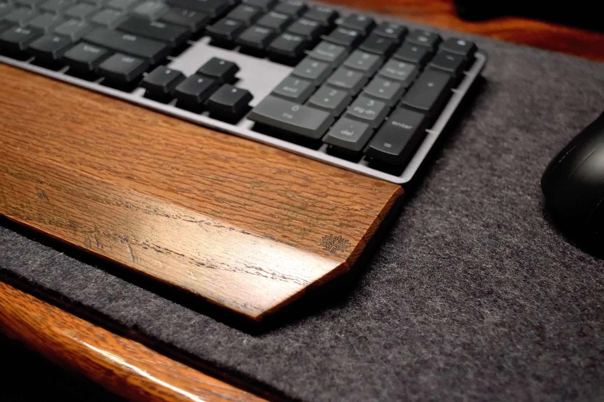 Black keyboard with a close up of a black-stained oak wrist rest on a dark wool desk pad.