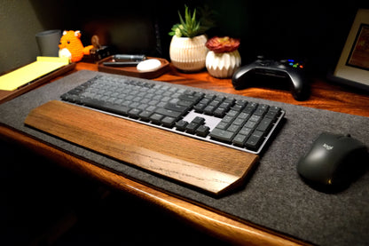 Keyboard on a desk with a Lonoke Designs black-stained keyboard wrist rest, black mouse, and other decorative items.
