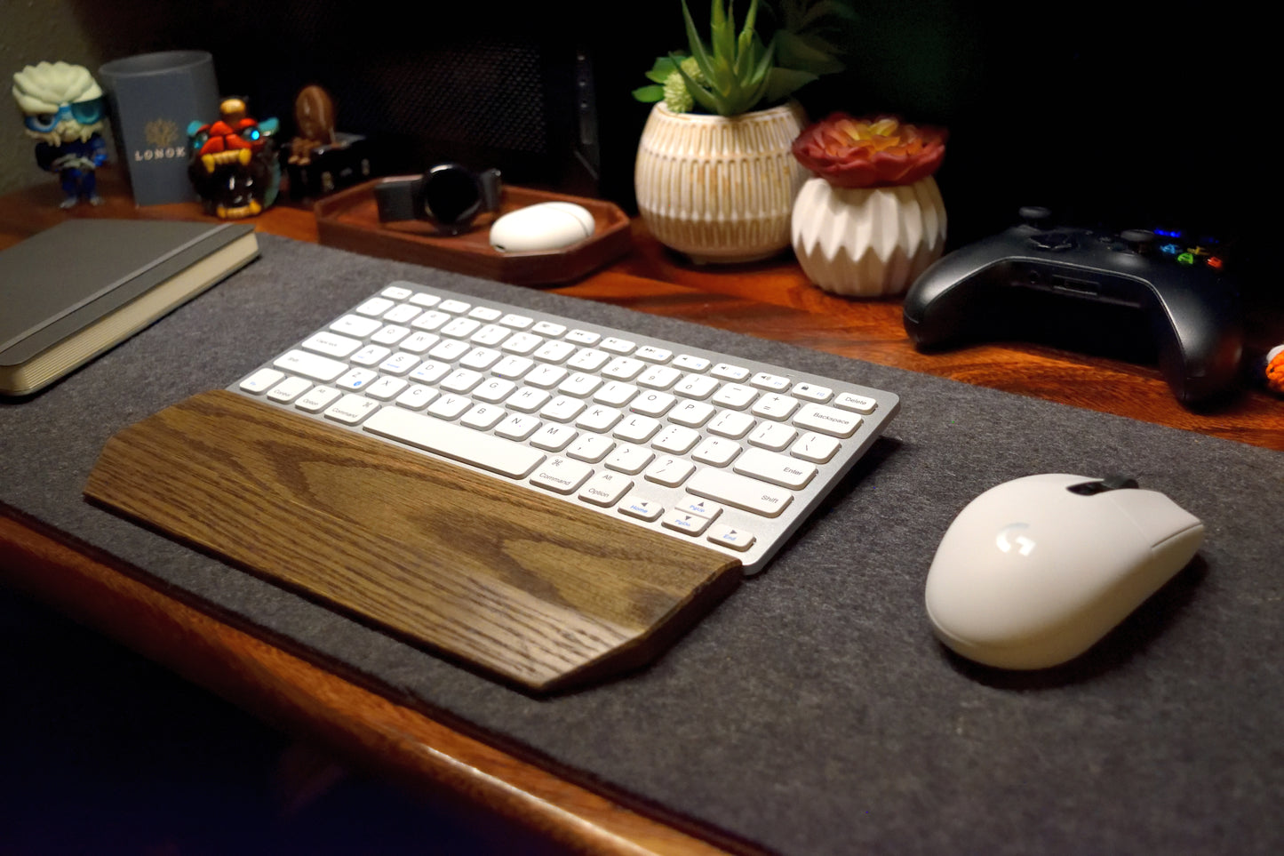 Keyboard with a Lonoke Designs black-stained oak wrist rest and mouse on a desk with decorative items.