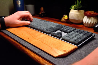 A person using a mechanical keyboard with a Lonoke Designs Cherry hardwood wrist rest on a desk.