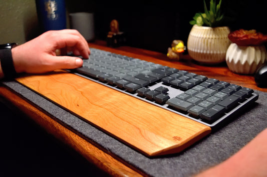 A person using a mechanical keyboard with a Lonoke Designs Cherry hardwood wrist rest on a desk.