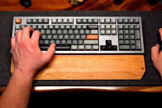 A person typing on a mechanical keyboard with a Lonoke Designs Cherry Hardwood wrist rest.