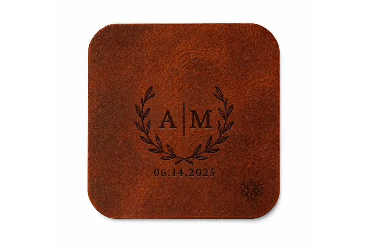 A Cognac brown veg-tanned leather square coaster with rounded corners, featuring a small Lonoke Designs logo in the bottom right corner, set against a plain white background. Featuring an example of a monogram custom laser engraving.
