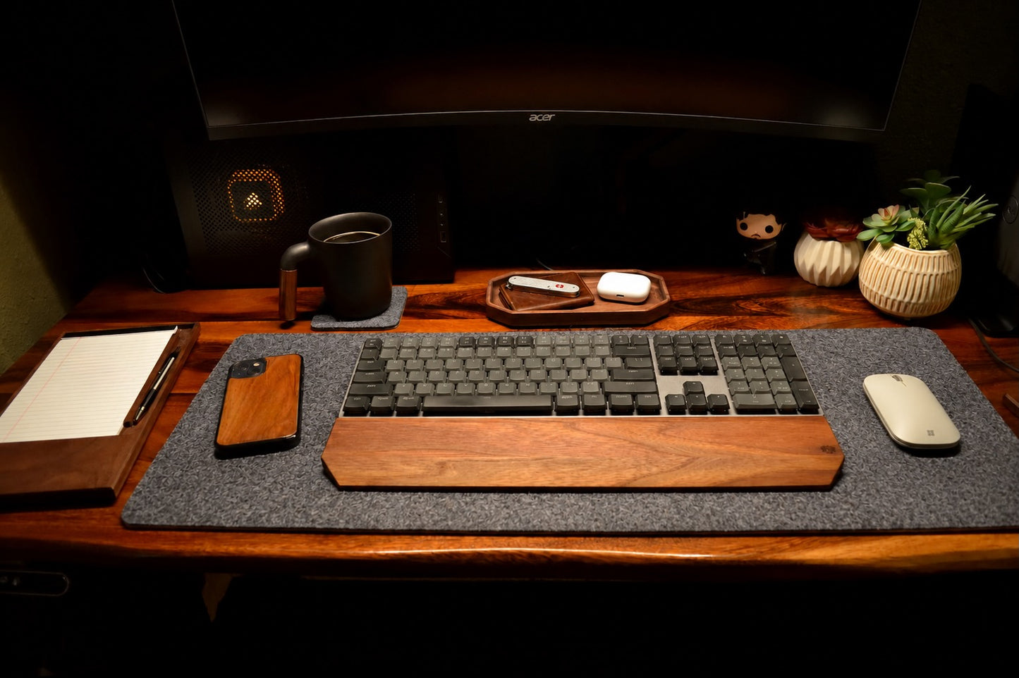 Wooden desk setup with keyboard, mouse, phone, and mug on a dark background