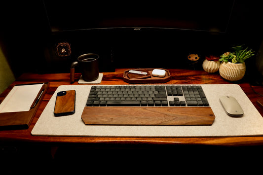 Wooden desk setup with keyboard, phone, mug, and small plants.