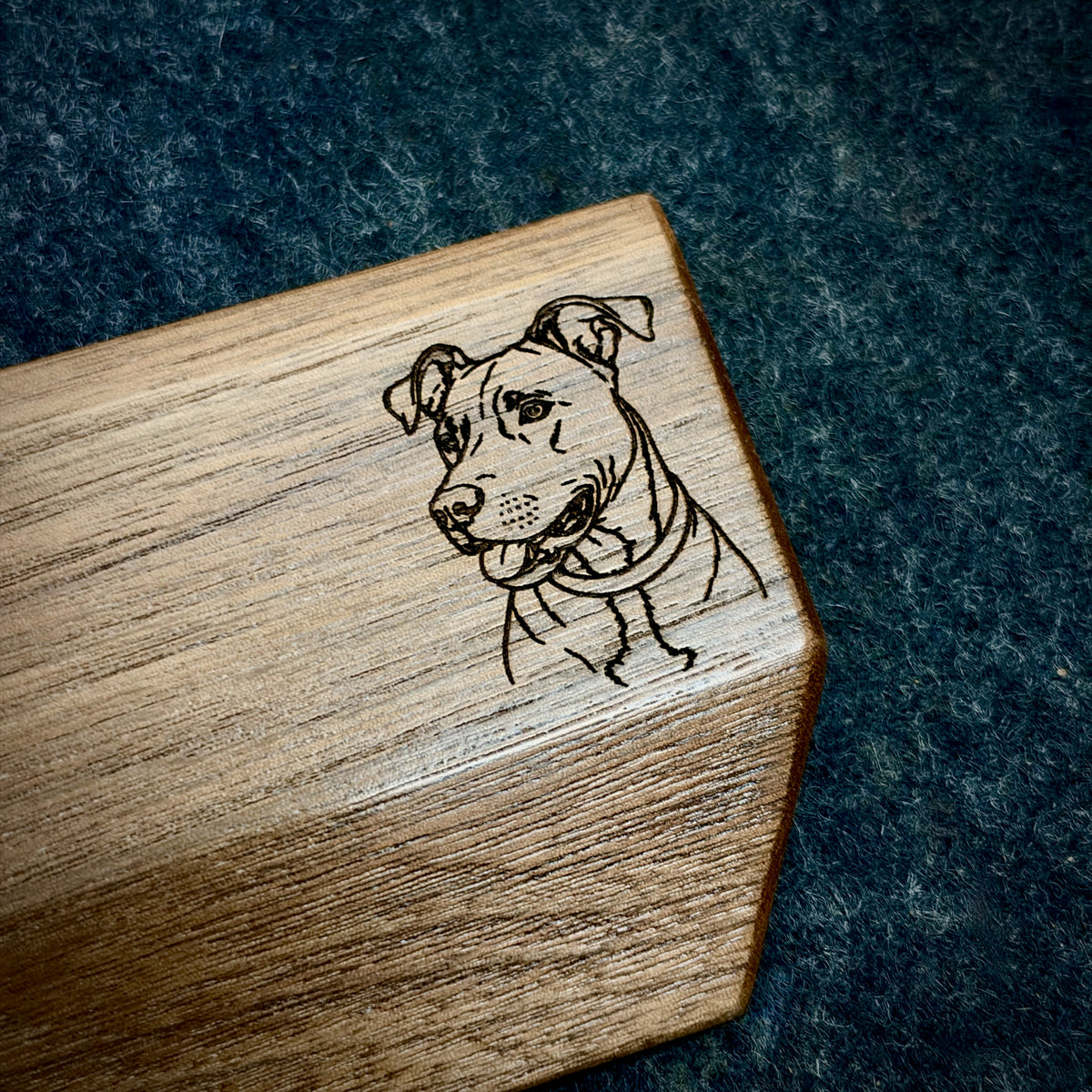 A close-up of a Lonoke Designs walnut wooden mechanical keyboard wrist rest corner featuring a custom laser-engraved portrait of a dog, set against a dark wool felt desk pad background.