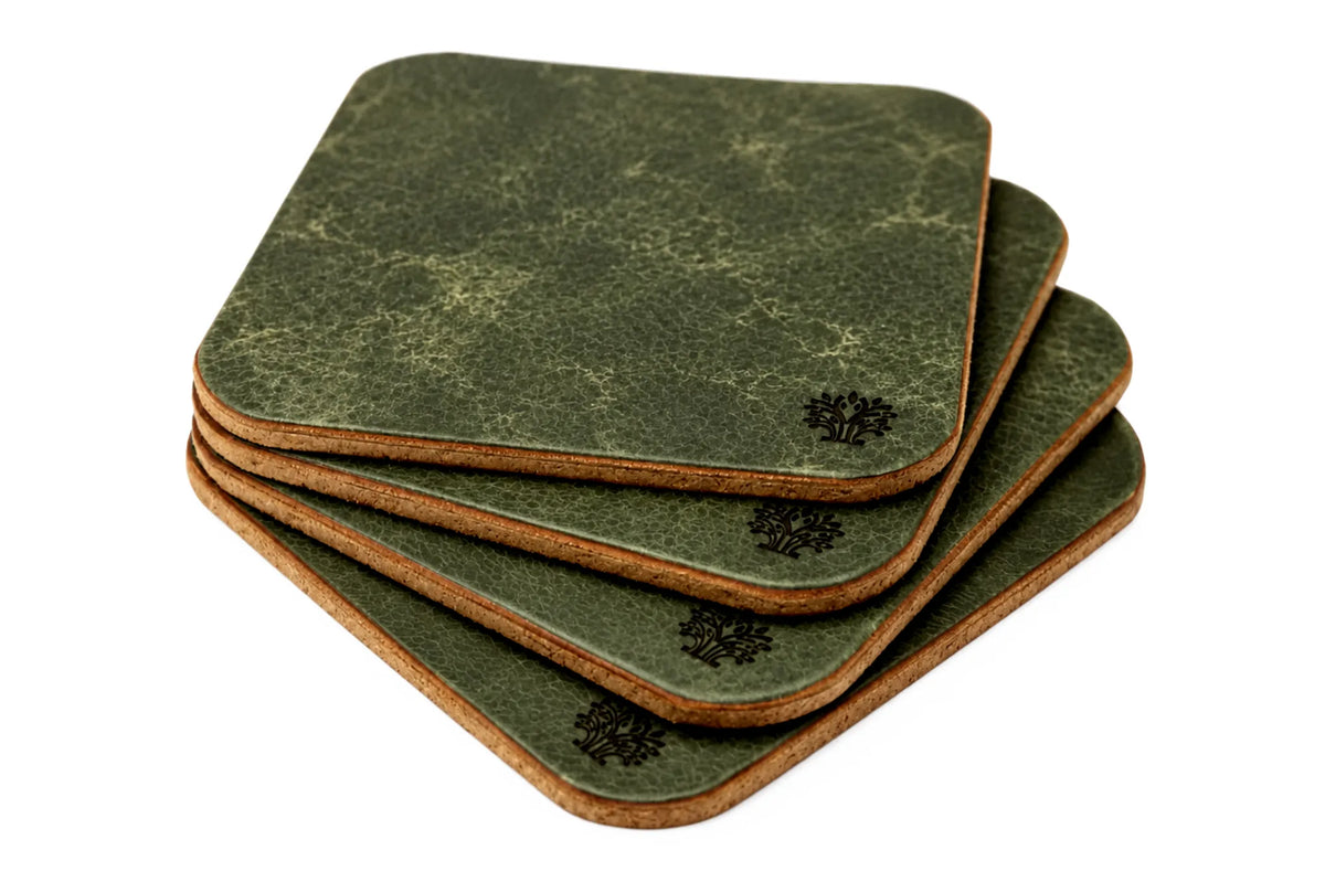A stack of four square coasters with rounded corners, featuring an Emerald green vegetable-tanned leather top surface and a natural cork bottom, with a small Lonoke Designs logo printed on the corner.
