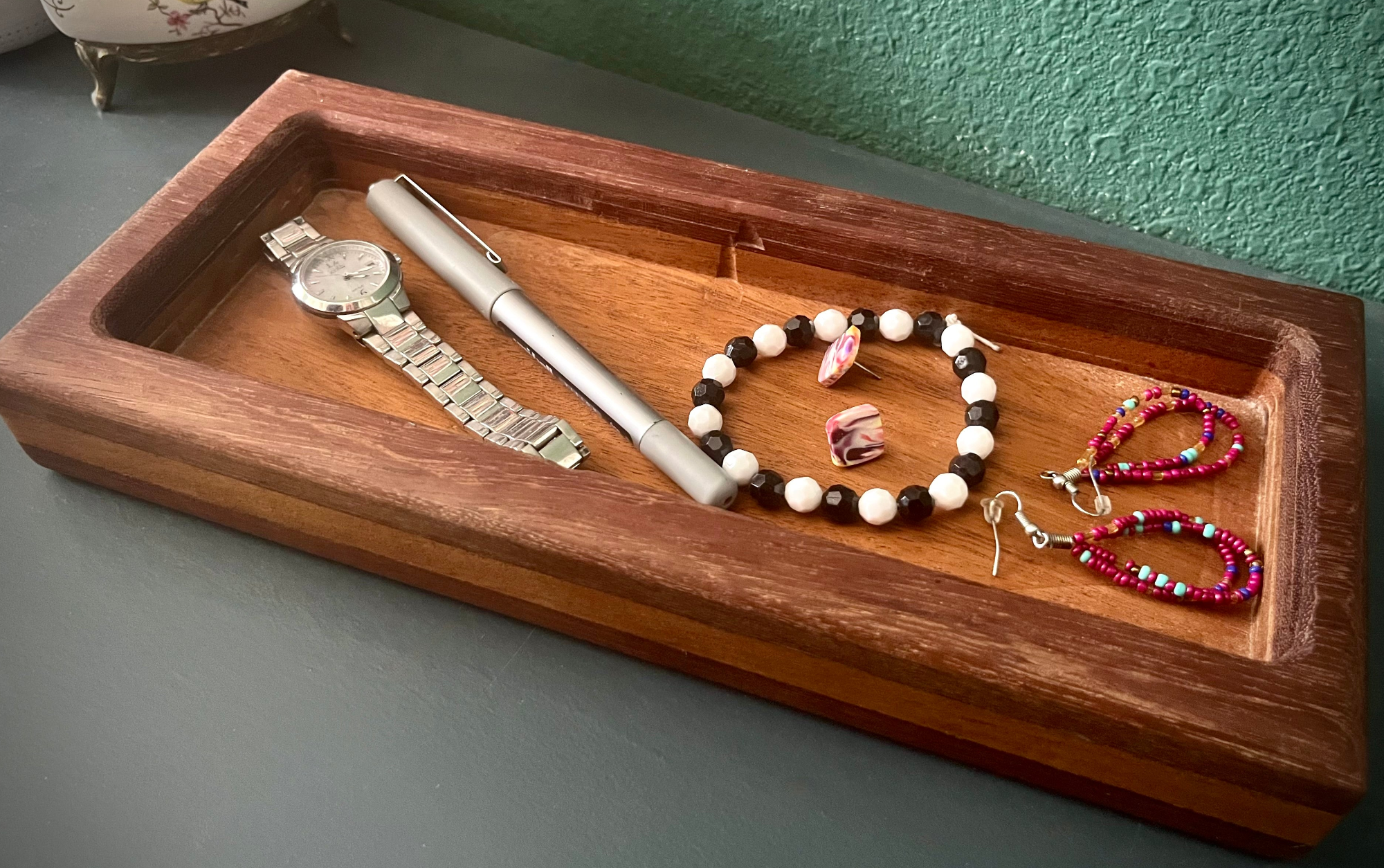 Wooden tray with jewelry and a pen on a gray surface