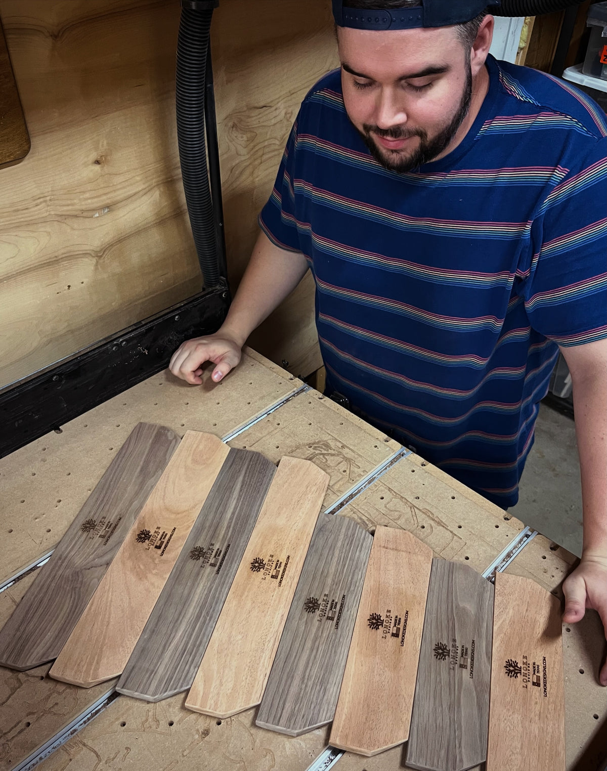 Jay is examining freshly milled and engraved Lonoke Designs hardwood mechanical keyboard wrist rests on a wooden surface.