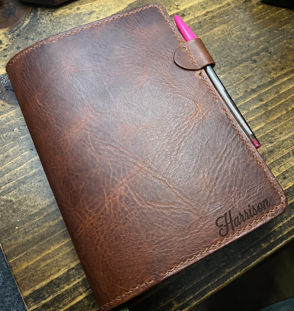 Brown leather Lonoke Designs Journal Cover with a pink pen on a wooden table.
