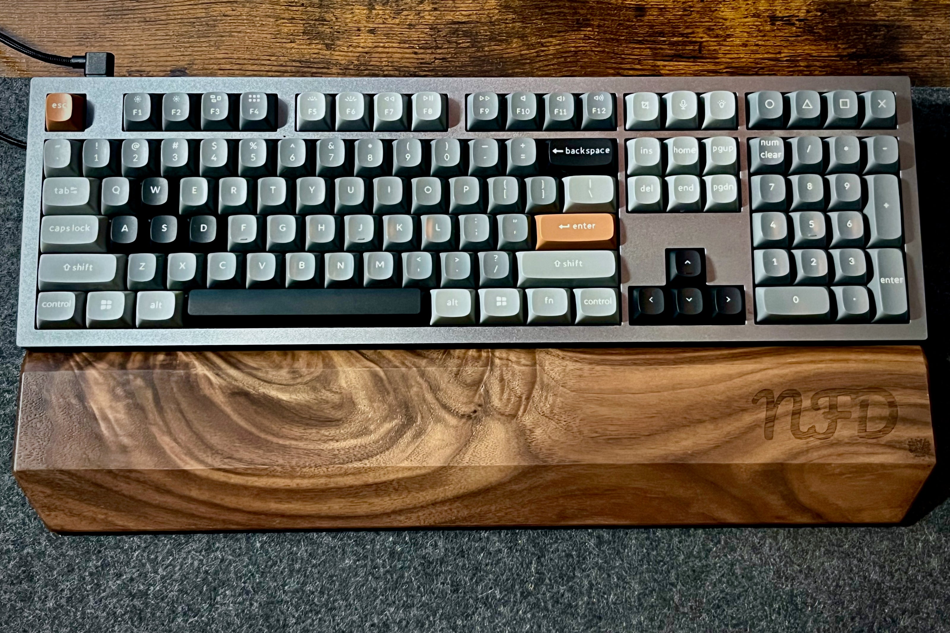 Mechanical keyboard with Walnut keyboard wrist rest, custom-engraved with initials. Sitting on a charcoal, wool felt and cork desk pad. Handcrafted and laser-engraved in-house at Lonoke Designs.