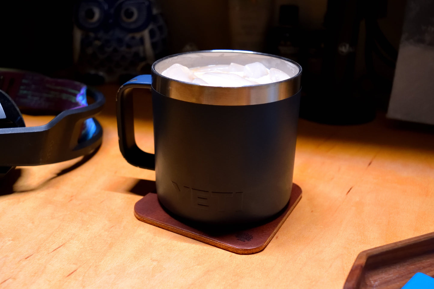 Navy stainless steel mug sitting on a Lonoke Designs Leather Coaster on a wooden des.