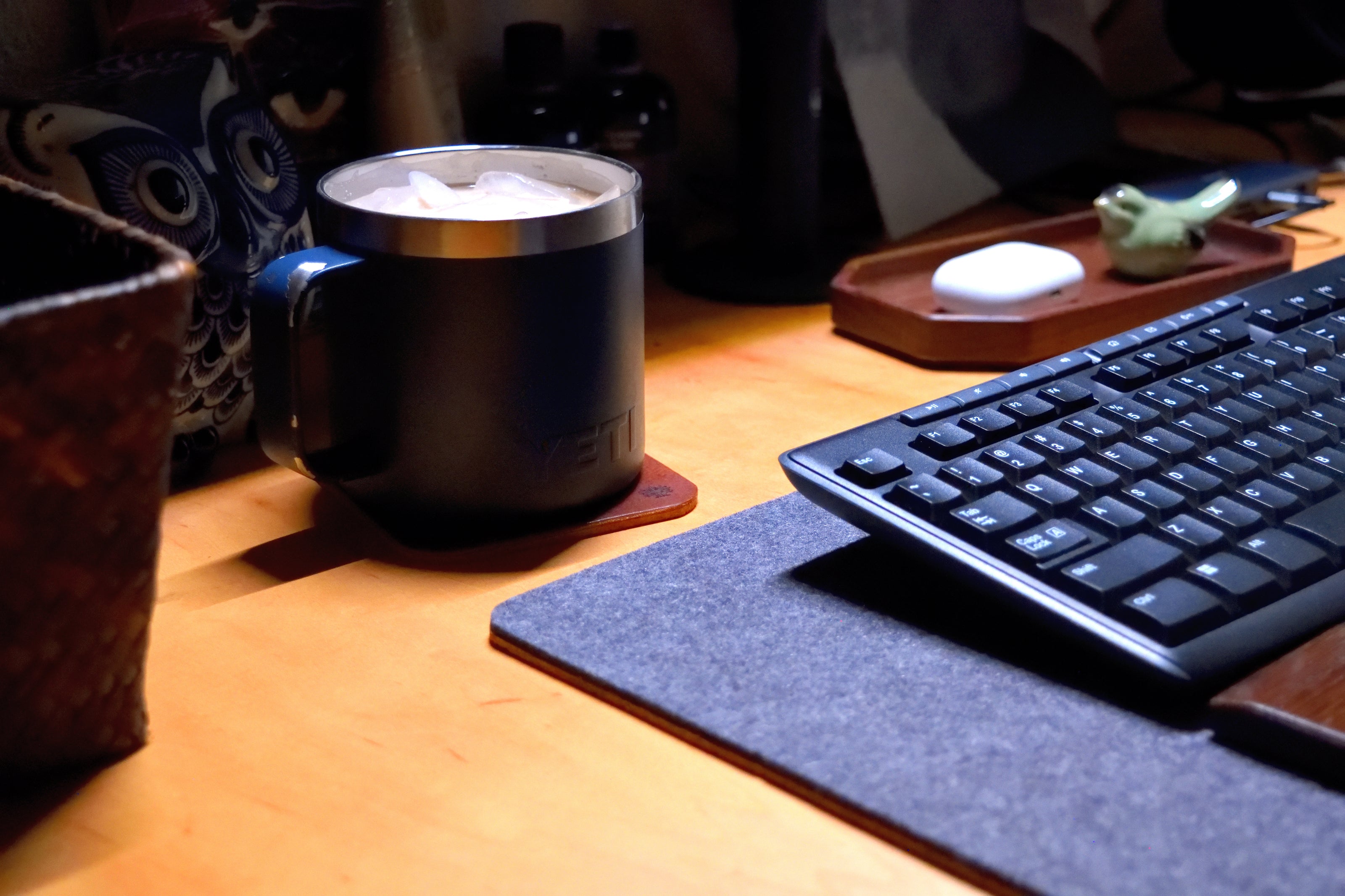 Blue mug on top sitting on a Lonoke Designs leather coaster. Resting on a wooden desk next to a keyboard and mouse.