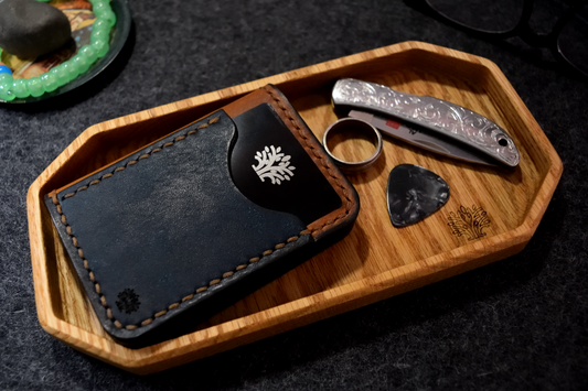Blue leather wallet with a tree logo on a wooden tray with a ring and pocket knife.