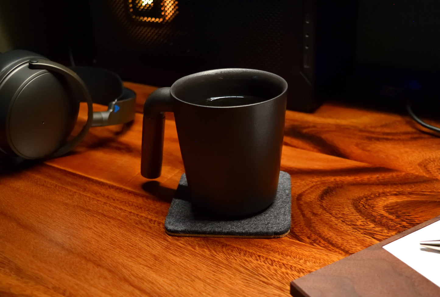 A square coaster made of wool felt and cork, displayed on a wooden surface with a black cup on top of it.