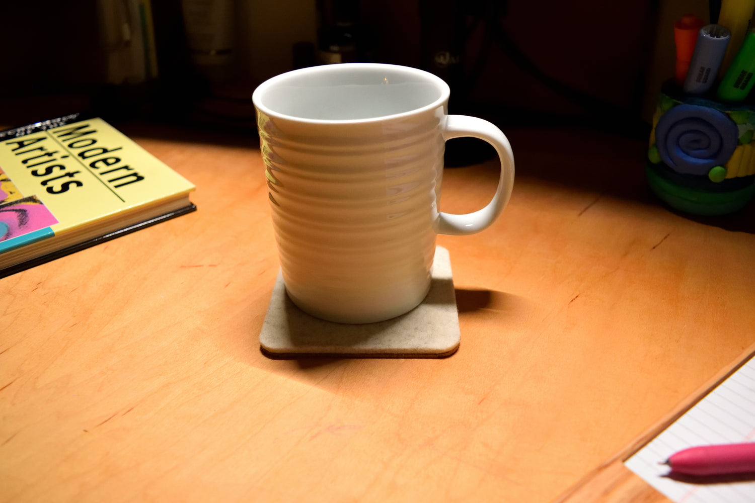 Wool white coaster with white mug, sitting on wood desk.