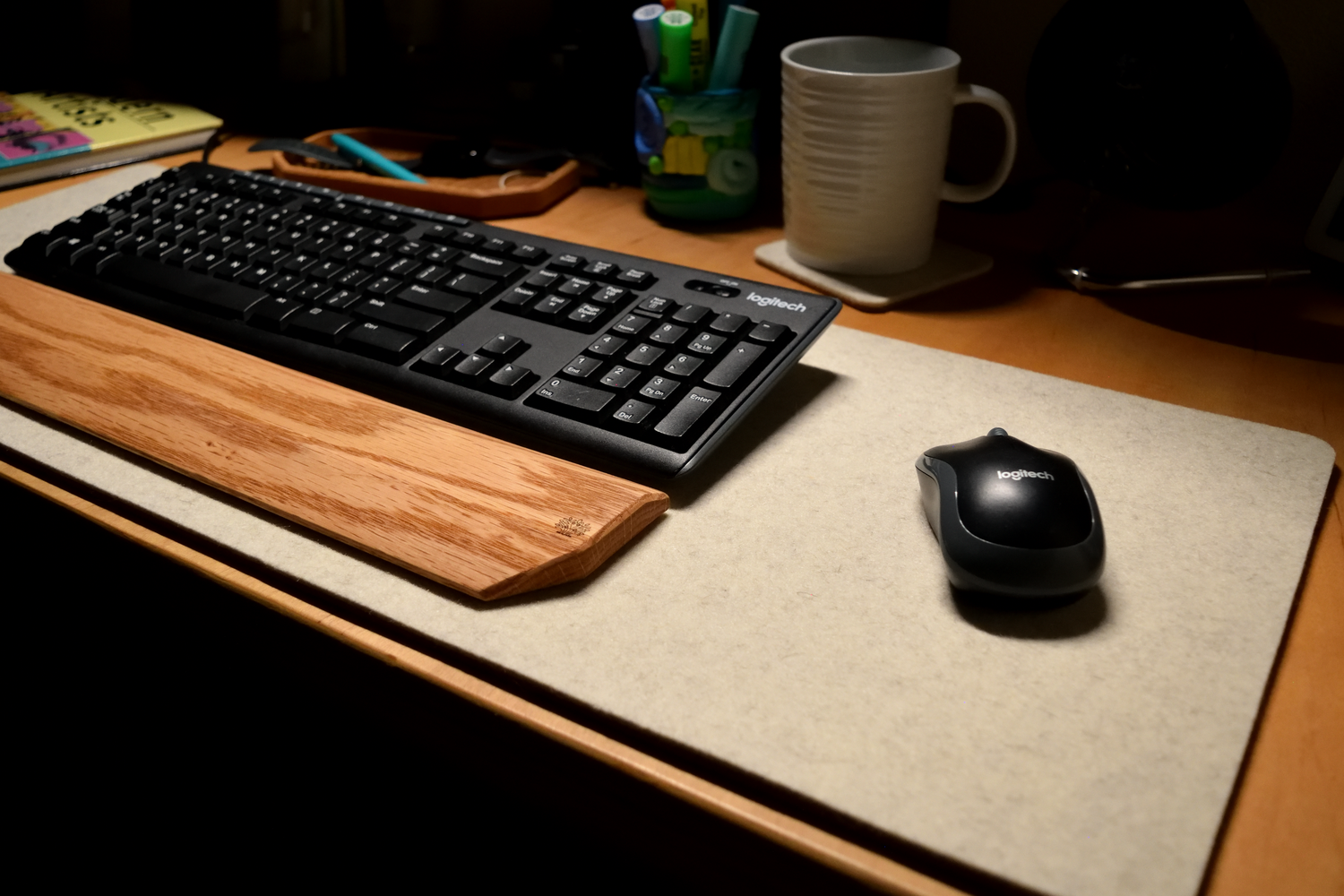Keyboard and mouse on a wool white desk pad with a mug and stationery items in the background