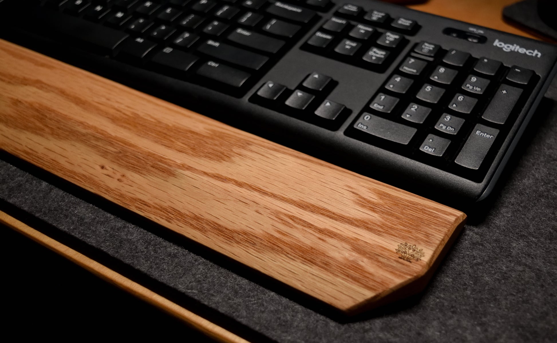 Keyboard on an oak wood wrist rest with a dark wool desk pad background.