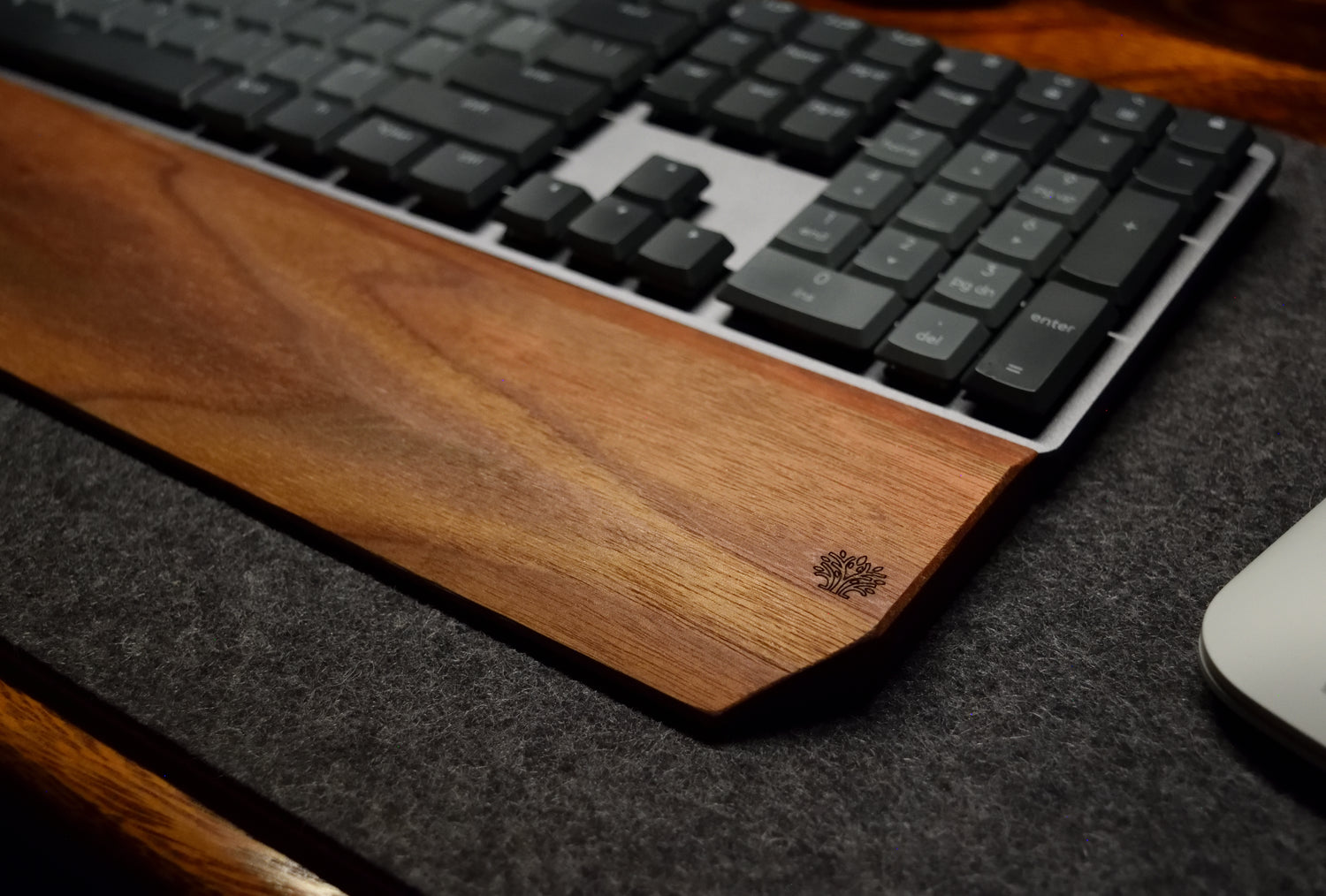 A walnut hardwood wrist rest placed on a wool desk pad with a keyboard and mouse.