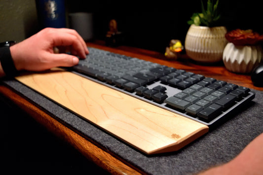 A person using a mechanical keyboard with a Lonoke Designs maple hardwood keyboard wrist rest on a desk.