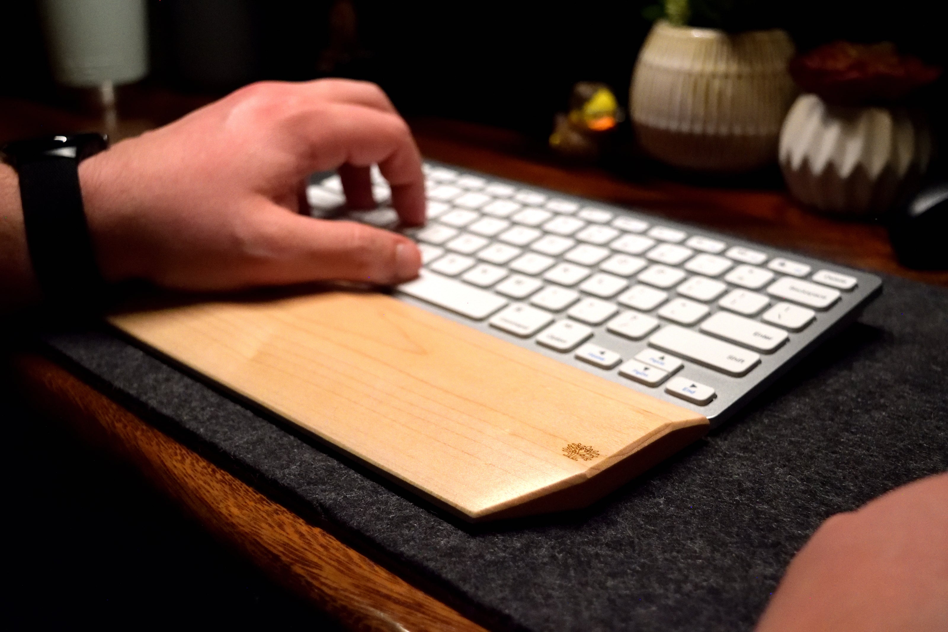 A mechanical keyboard with a Lonoke Designs Maple hardwood wrist rest on a dark wool desk pad.