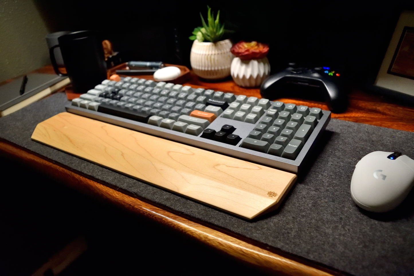 A mechanical keyboard on a desk with a Lonoke Designs Maple Hardwood wrist rest, mouse, and other office items.