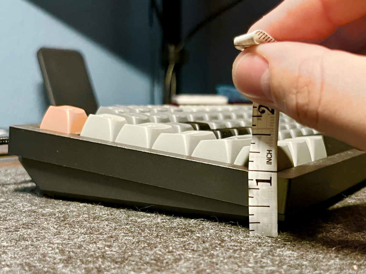 Hand holding a small measuring tool next to a mechanical keyboard on a charcoal wool felt and cork desk pad by Lonoke Designs.