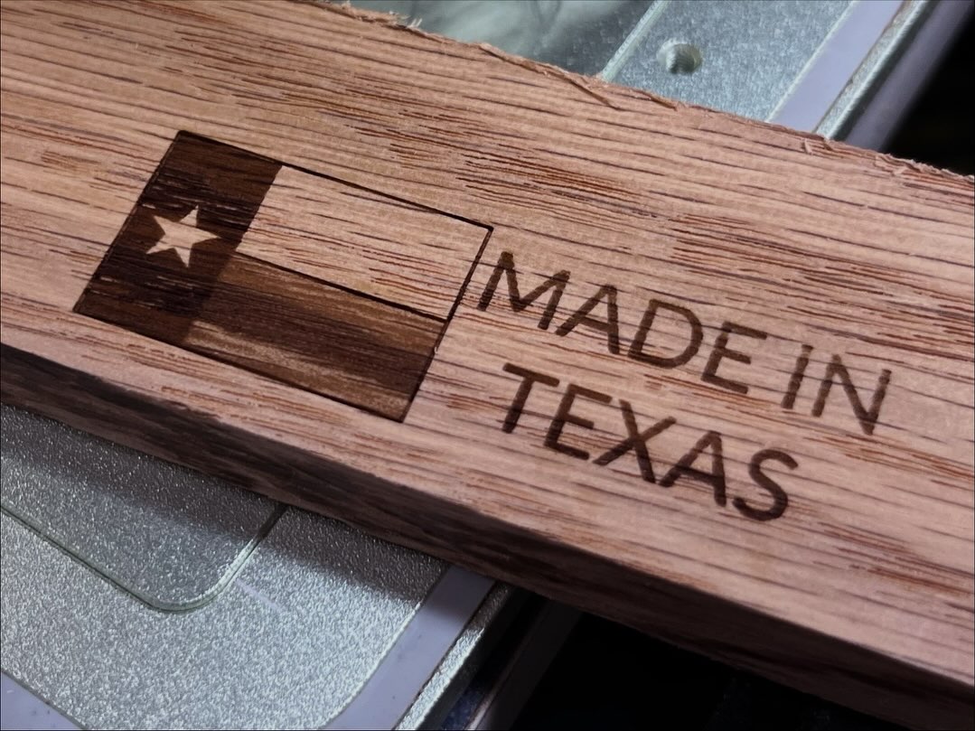 A close-up of a wooden sign or plaque engraved with the Texas flag and the words “MADE IN TEXAS,” resting on a metallic surface.