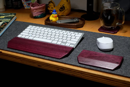 A wireless keyboard and mouse set with dark reddish-brown wooden wrist rests and palm bars, placed on a gray desk mat on a wooden desk.