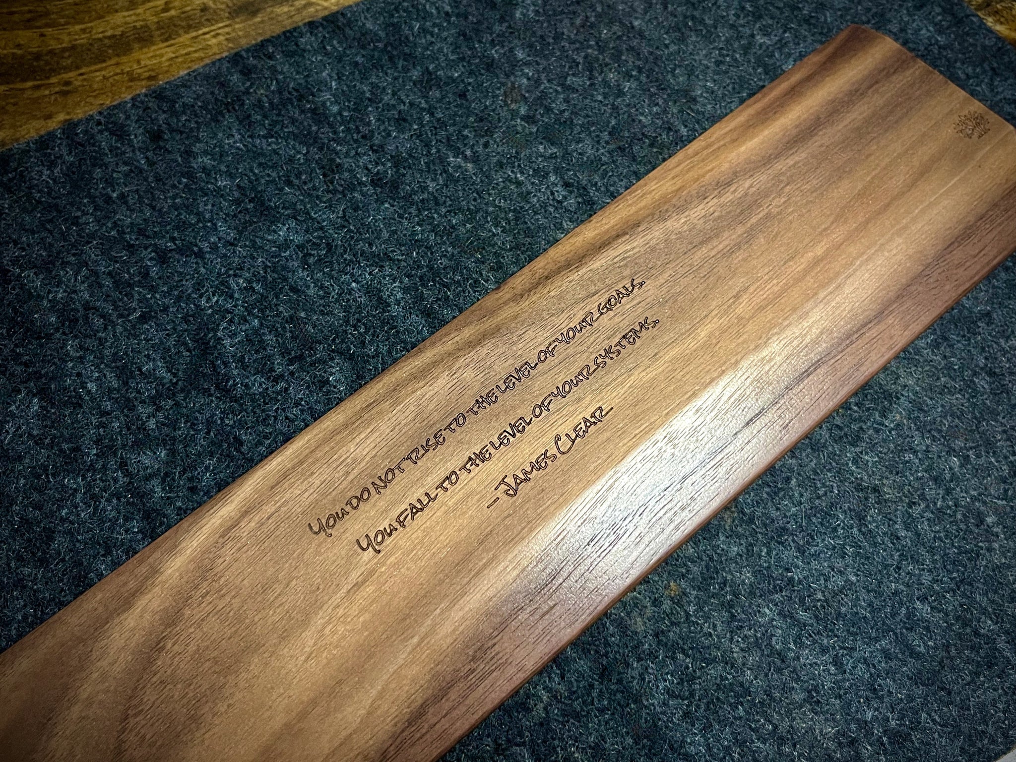 Walnut keyboard wrist rest handcrafted by and custom engraved with a quote by Lonoke Designs. It is resting on a gray wool felt desk pad.