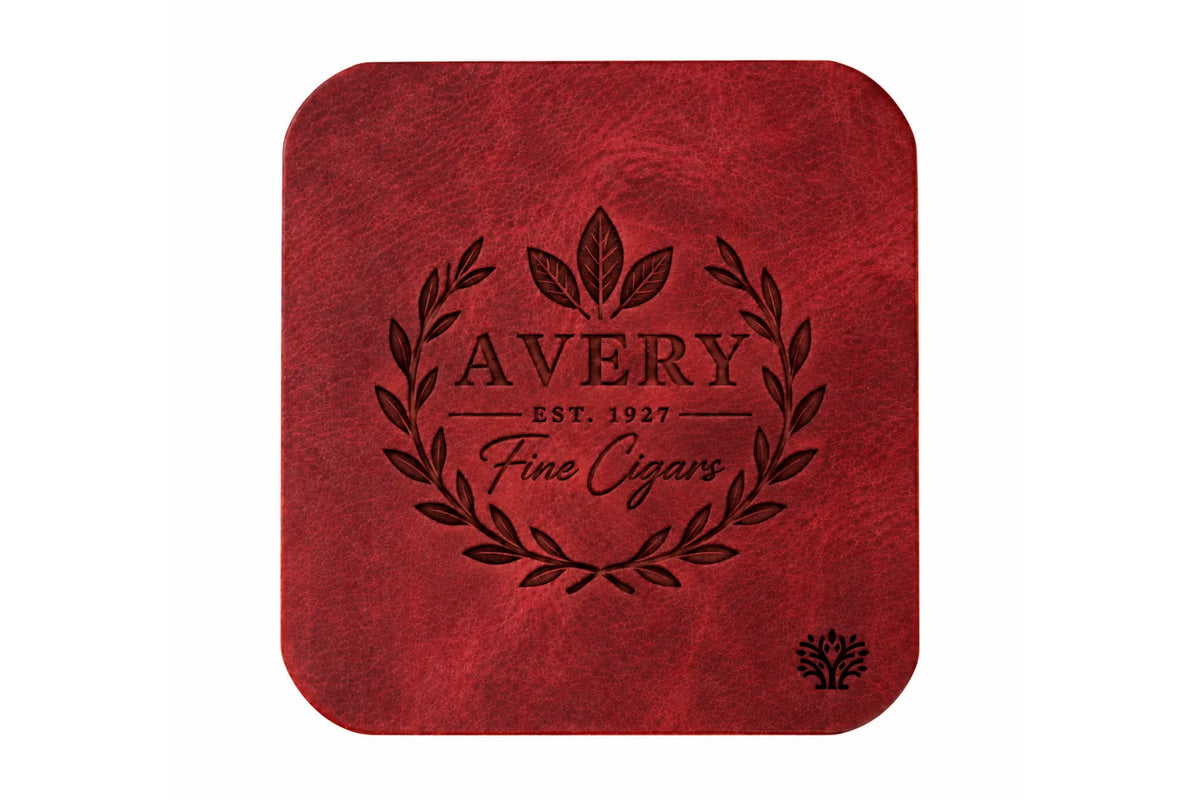 A Ridglea Rouge red veg-tanned leather square coaster with rounded corners, featuring a small Lonoke Designs logo in the bottom right corner, set against a plain white background. Featuring an example of a company's custom laser engraving.