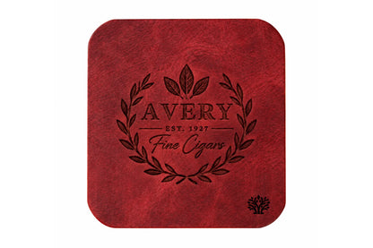 A Ridglea Rouge red veg-tanned leather square coaster with rounded corners, featuring a small Lonoke Designs logo in the bottom right corner, set against a plain white background. Featuring an example of a company's custom laser engraving.