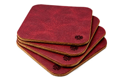 A stack of four square coasters with rounded corners, featuring a Ridglea Rouge red vegetable-tanned leather top surface and a natural cork bottom, with a small Lonoke Designs logo printed on the corner.