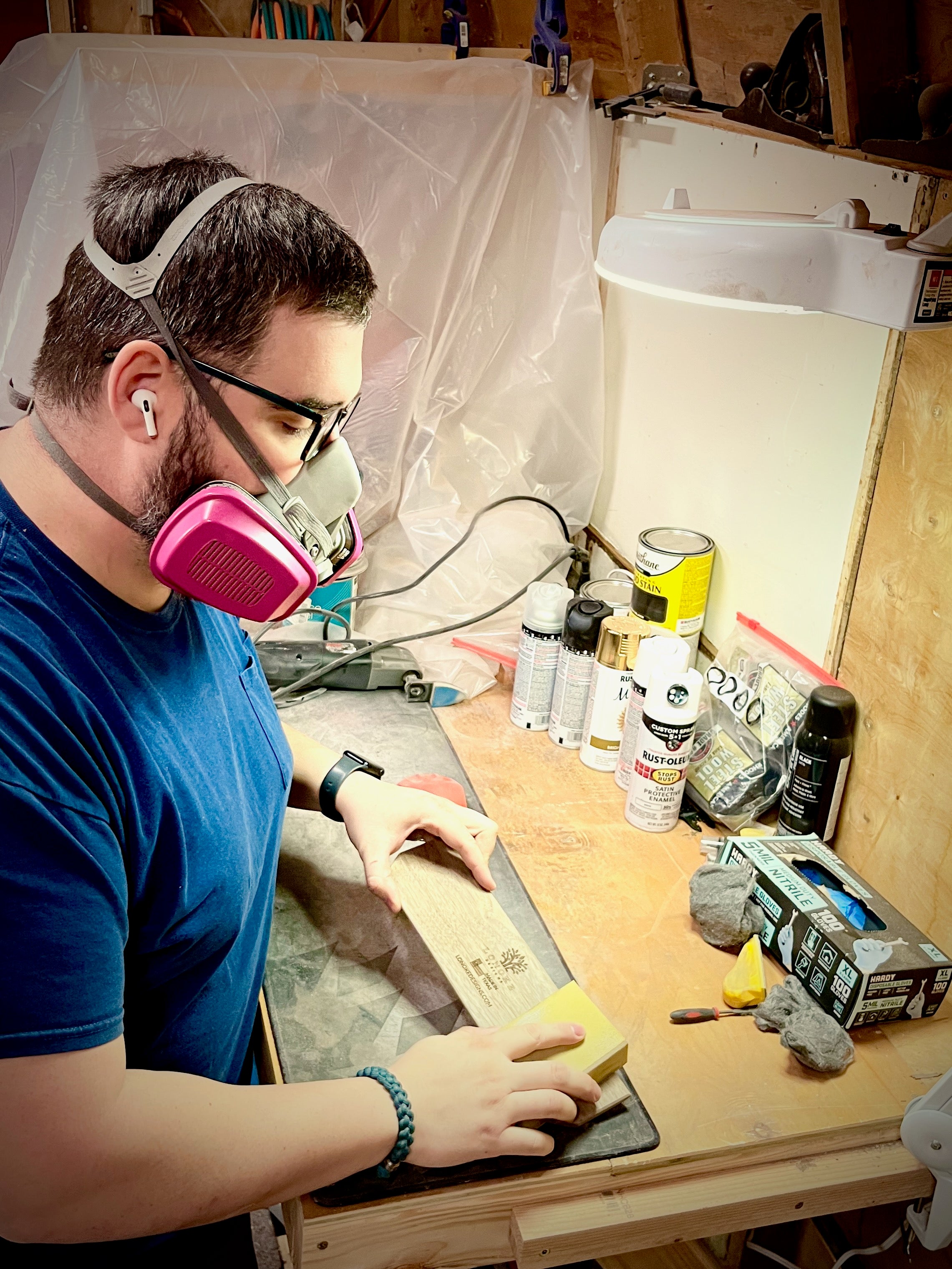 Person wearing a respirator mask working at a wooden table with various items in a workshop.