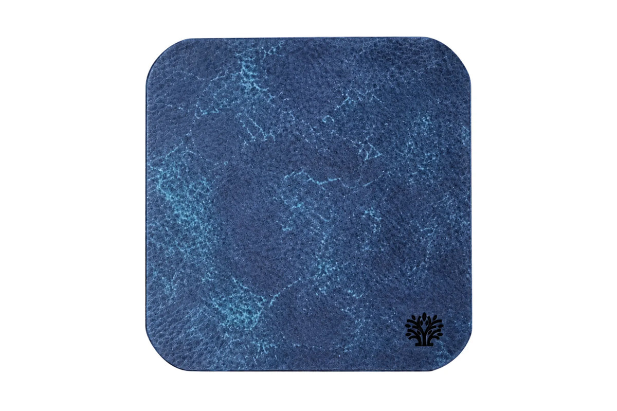 A Sapphire blue veg-tanned leather square coaster with rounded corners, featuring a small Lonoke Designs logo in the bottom right corner, set against a plain white background.