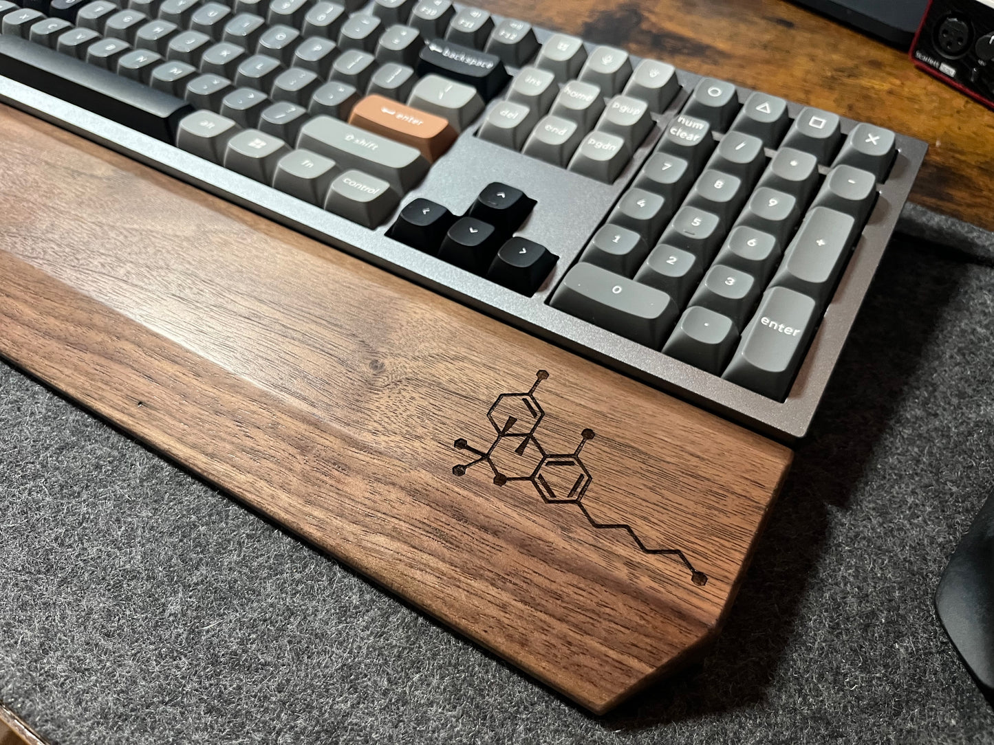 Mechanical keyboard with Walnut keyboard wrist rest, custom-engraved with a molecule. Sitting on a charcoal, wool felt and cork desk pad. Handcrafted and laser-engraved in-house at Lonoke Designs.