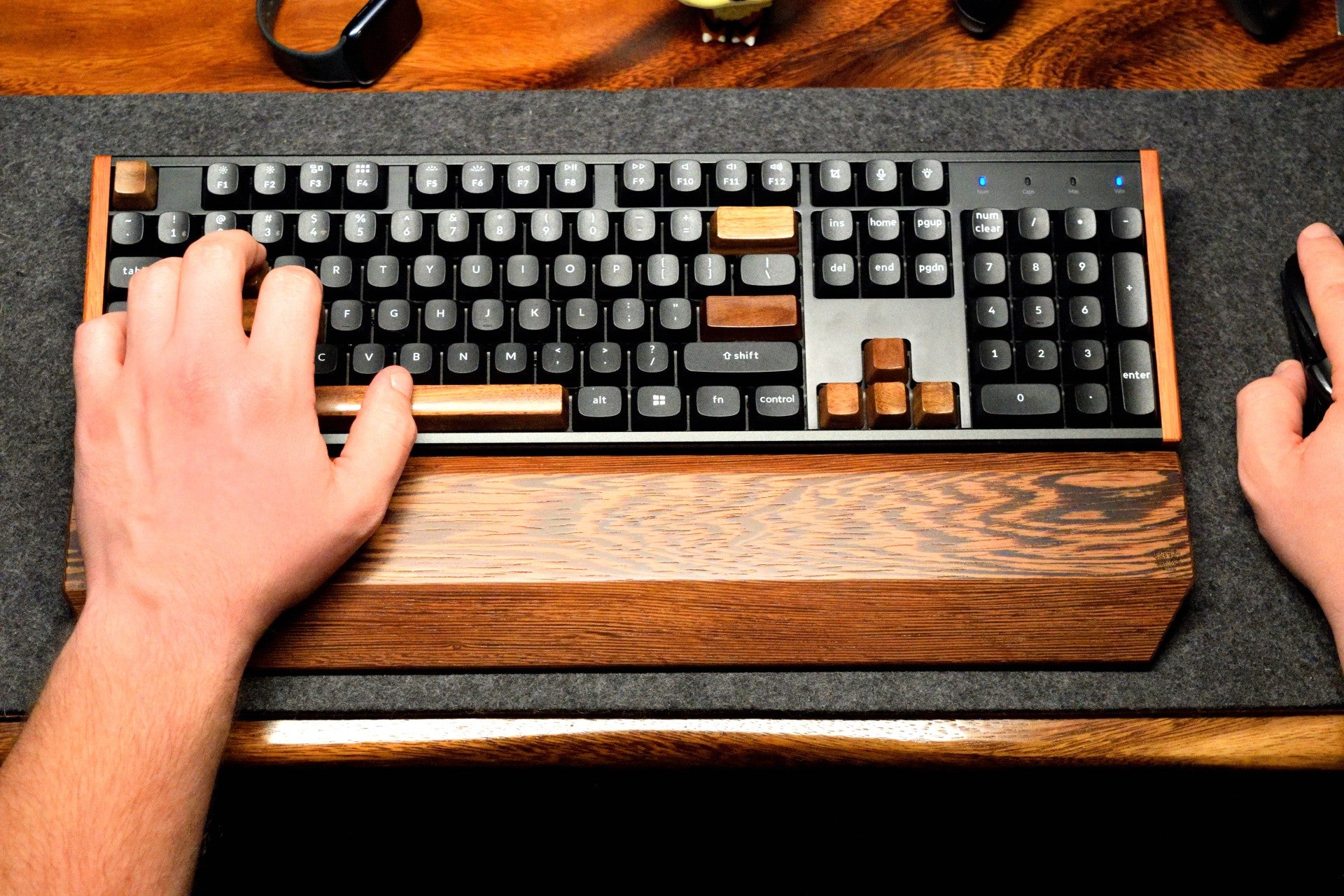 Person typing on a mechanical keyboard with a Lonoke Designs wenge hardwood wrist rest and mouse on a desk.
