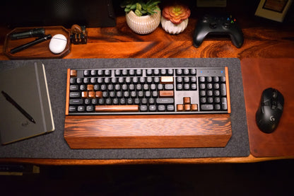 Mechanical keyboard with a Lonoke Designs wenge hardwood wrist rest on a gray wool desk pad with a mouse and other items.