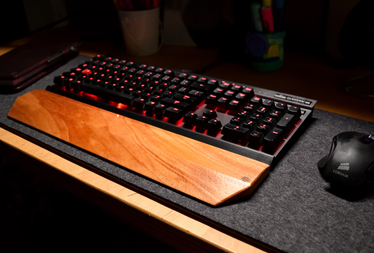 Gaming keyboard with a Lonoke Designs Mahogany wood mechanical keyboard wrist rest on a shadow gray wool felt desk pad.
