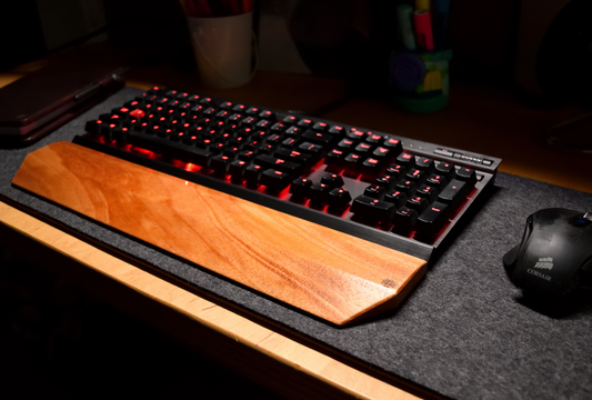 Gaming keyboard with a Lonoke Designs Mahogany wood mechanical keyboard wrist rest on a shadow gray wool felt desk pad.