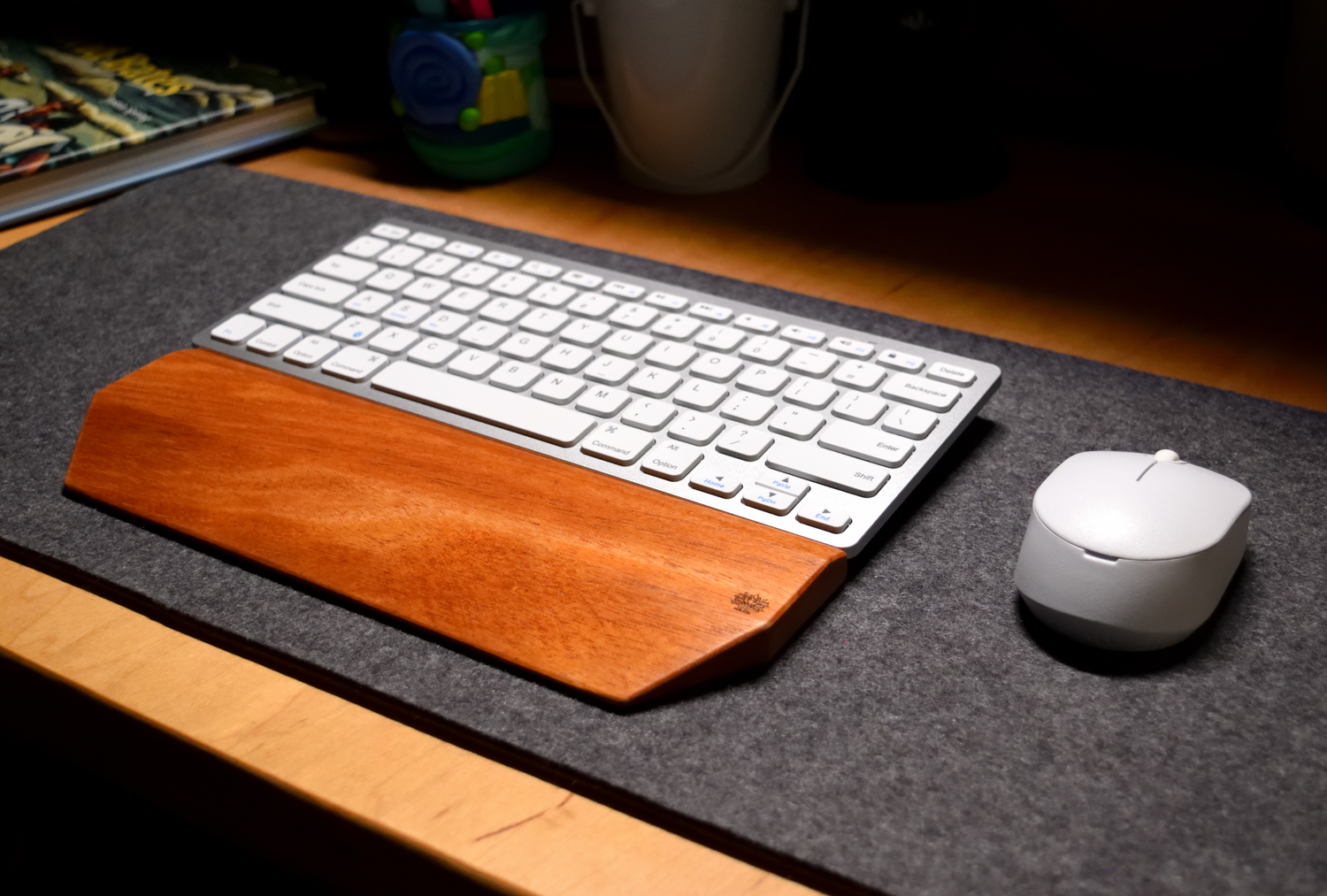Keyboard with a Lonoke Designs mahogany wood wrist rest and mouse on a gray wool desk pad.