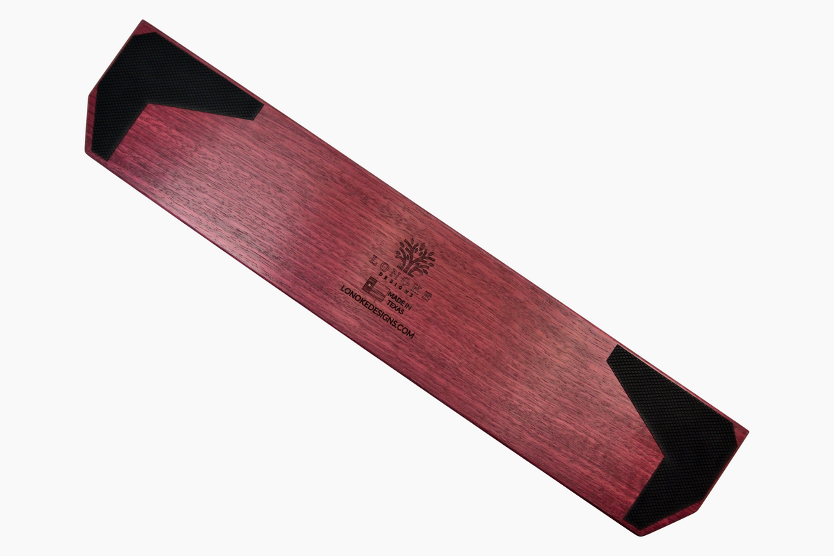 A Lonoke Designs Purpleheart wood mechanical keyboard wrist rest shown from a backsid angle to highlight the black rubber, anti-slip feet on a solid white background.