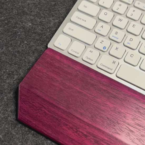 A video of a desk setup with a purpleheart wrist rest showcased with a white and silver keyboard on a charcoal wool felt and cork desk pad.