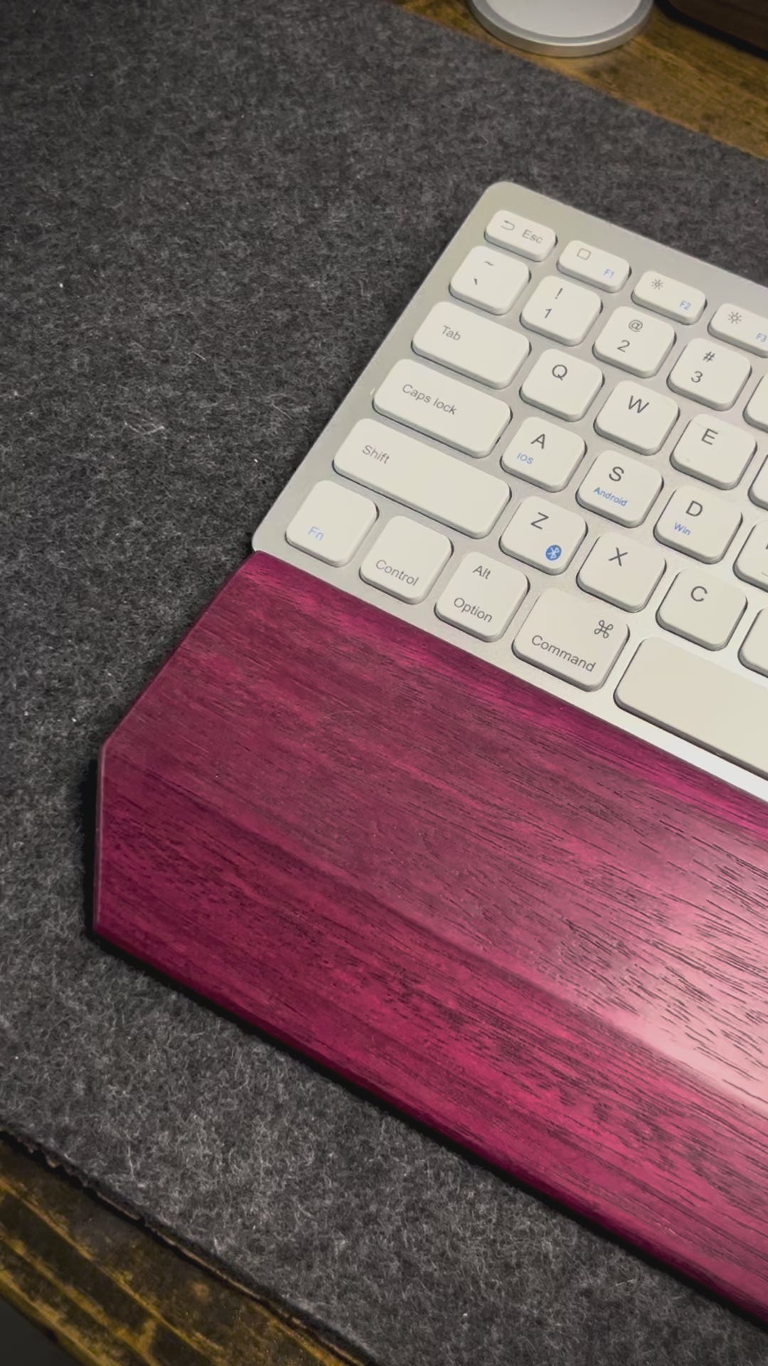 A video of a desk setup with a purpleheart wrist rest showcased with a white and silver keyboard on a charcoal wool felt and cork desk pad.