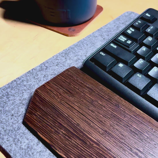 A video of a desk setup with a wenge wrist rest showcased with a black keyboard on a charcoal wool felt and cork desk pad.
